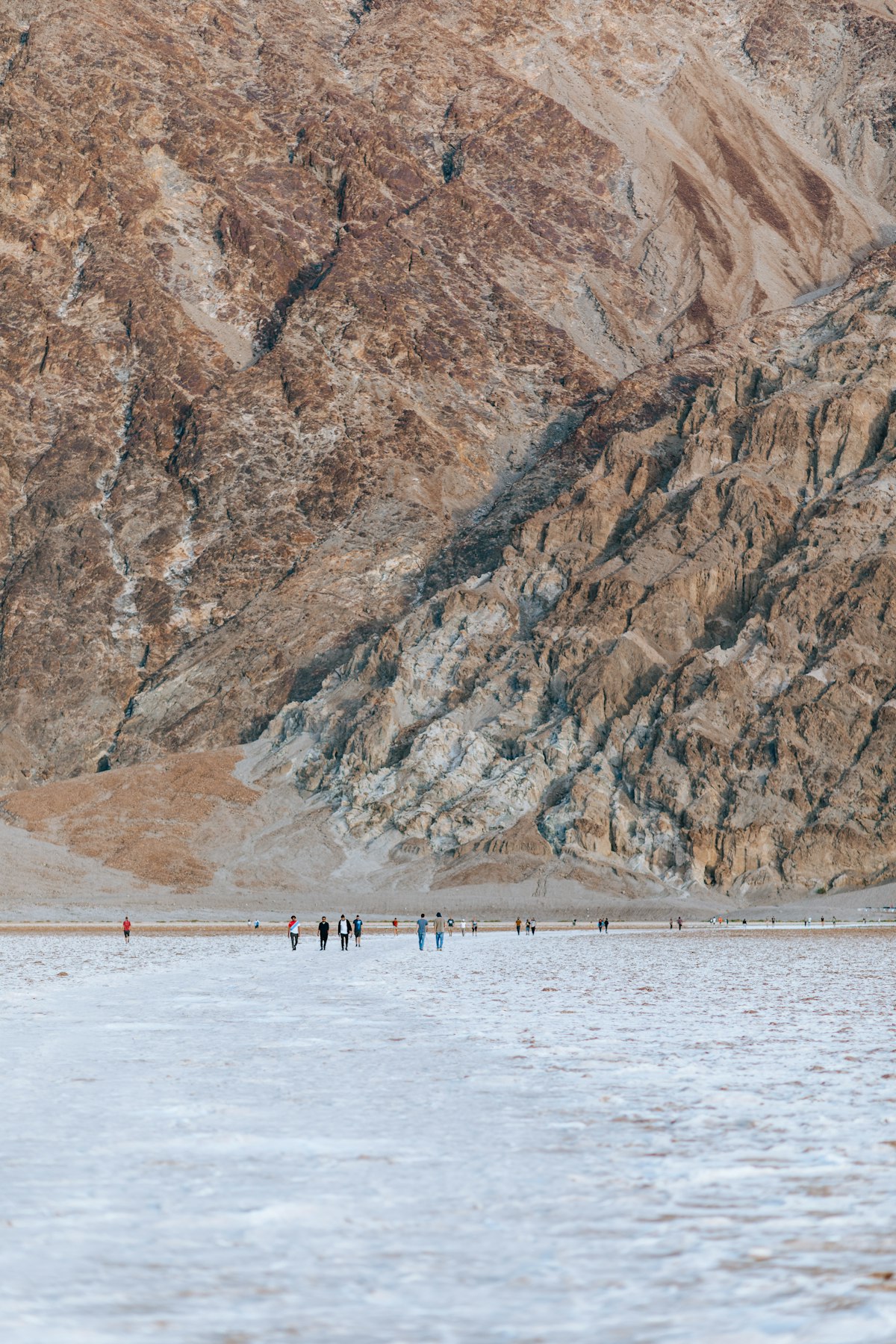 Hikers crossing the salt flats of Death Valley beneath a mountain face